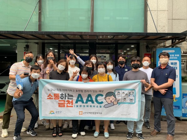 독산1동 주민센터 건물 앞에서 소통하는 금천, AAC 현수막 들고 사진 찍는 종사자들의 모습