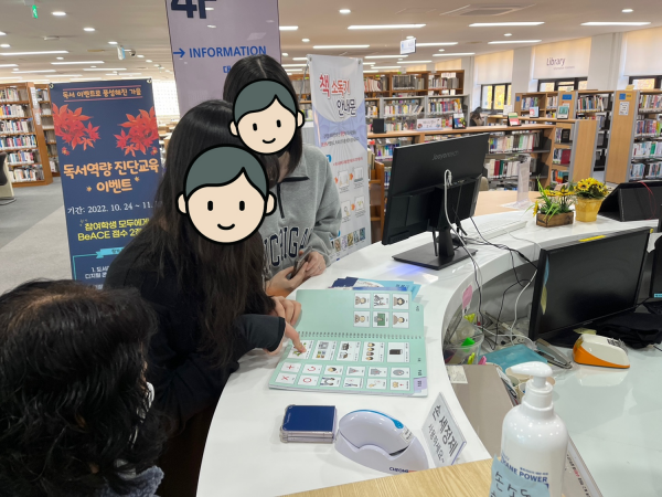 학교 내 도서관에서 책이 어디에 위치해 있는지 그림글자판으로 물어보는 학생