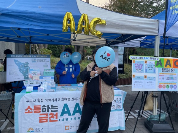 AAC 풍선을 들고 체험부스 앞에 서있는 이용자
