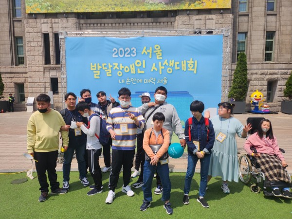 시울시청 앞 녹색광장에 설치된 서울발달장애인 사생대회 홍보벽 앞에서 찍은 이룸, 라온 아카데미 이용자 단체사