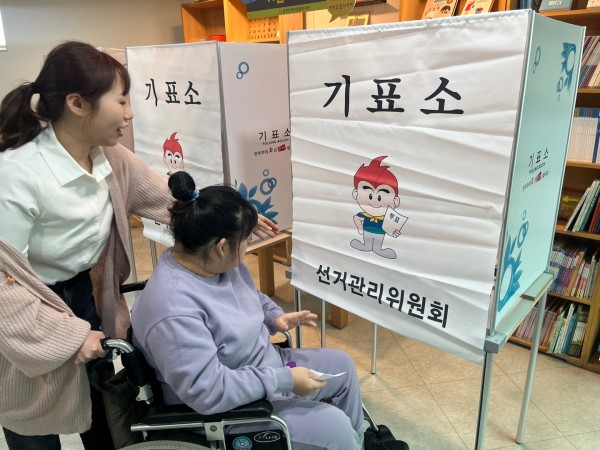 휠체어 이용인분이 투표에 참석하실 수 있도록 지원하고 있는 사회복지사의 모습