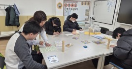 책상에 둘러앉아 강사님께 미술 수업을 받는 청소년들