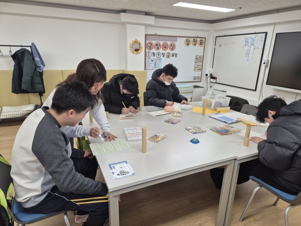 책상에 둘러앉아 강사님께 미술 수업을 받는 청소년들